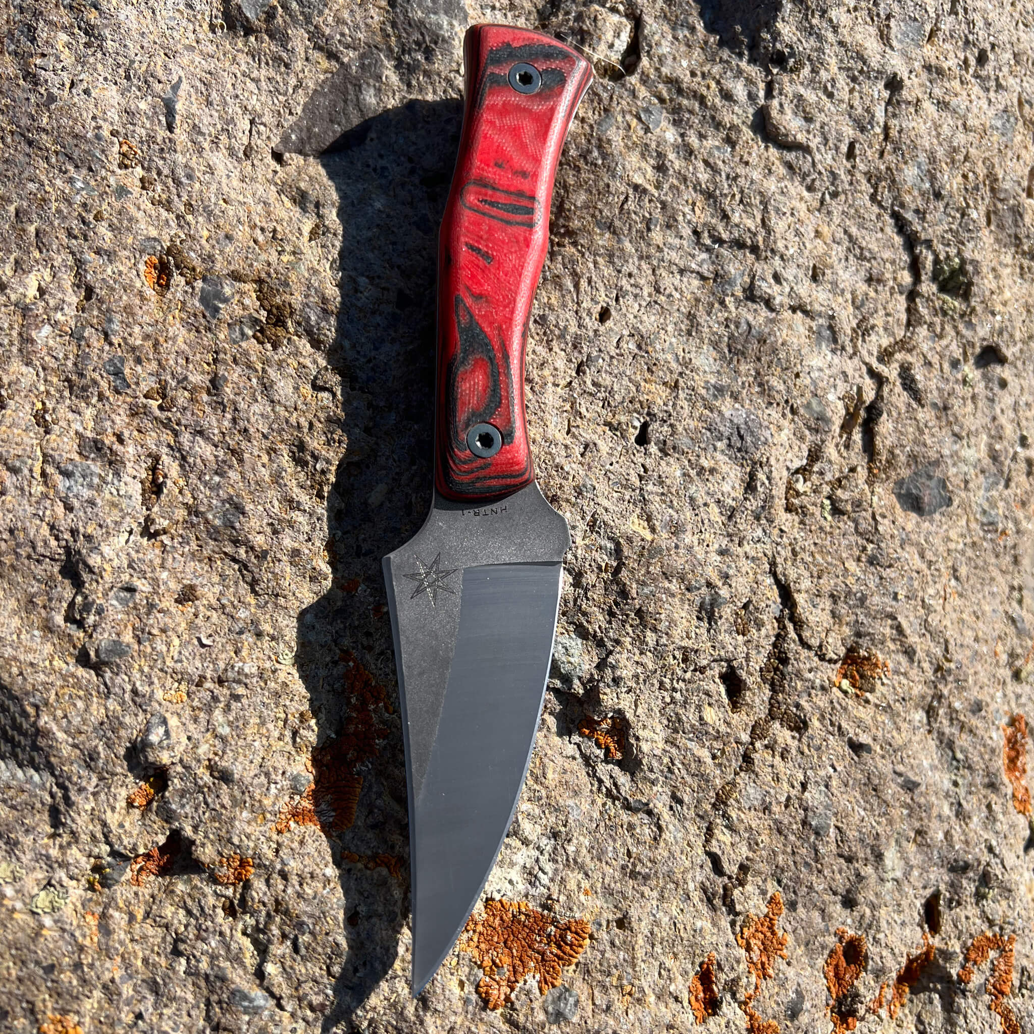 Hunting Knife with a red and black handle on a textured stone surface