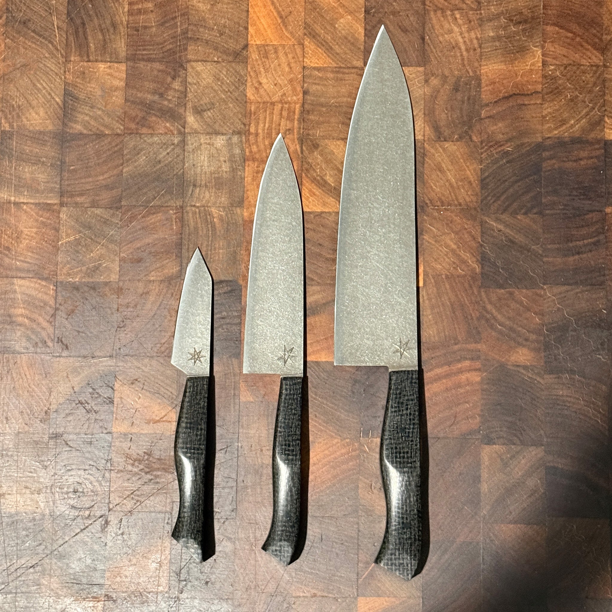 Set of three kitchen knives with black textured handles on a wooden surface