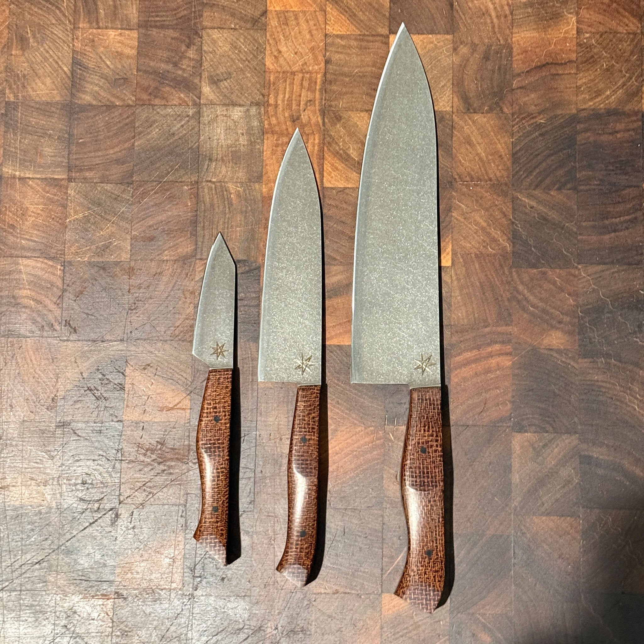 Set of three kitchen knives with brown handles on a wooden surface